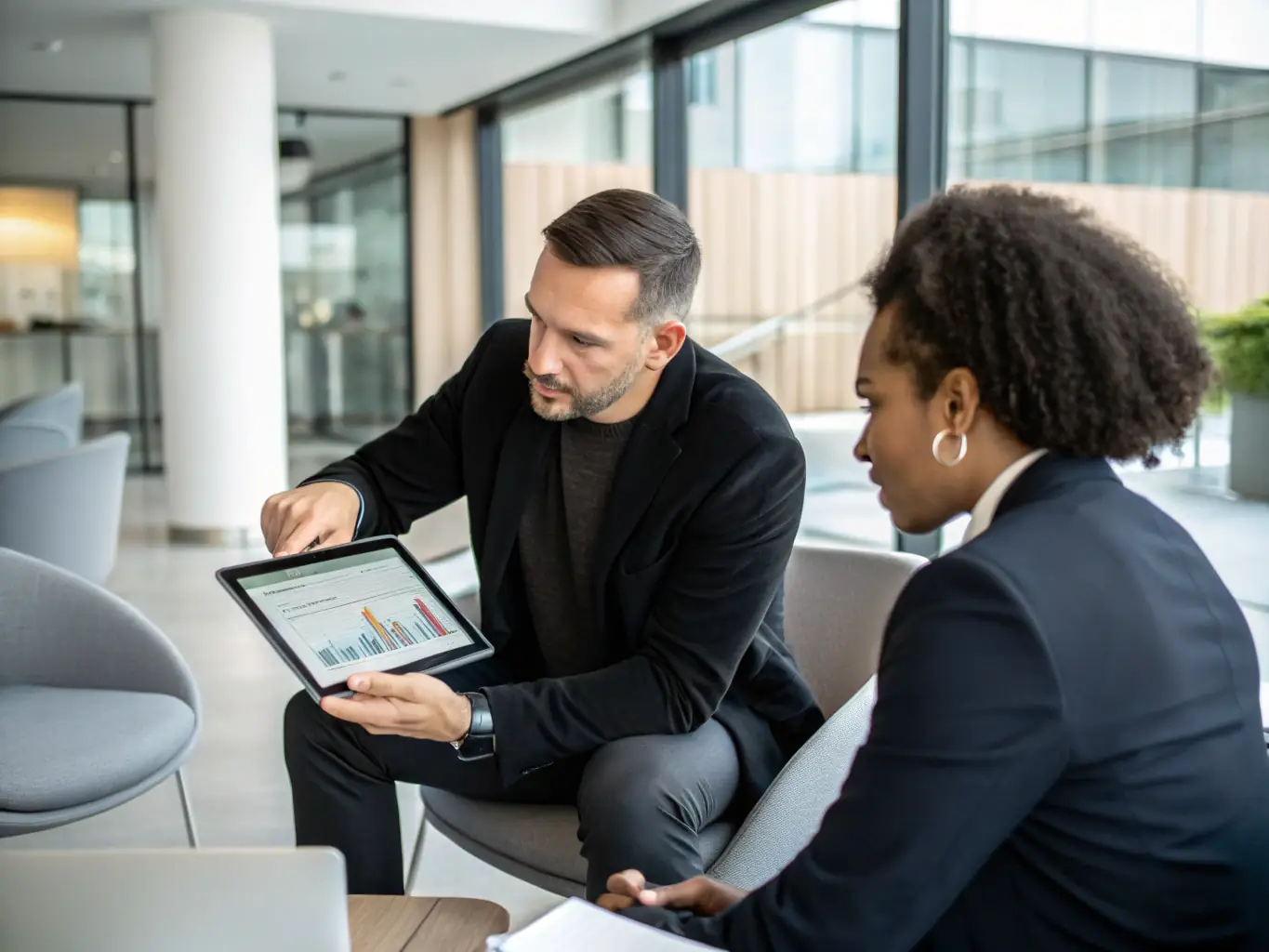 A photo of a consultant advising a client in a modern office, with charts and graphs visible in the background, symbolizing strategic planning and support.
